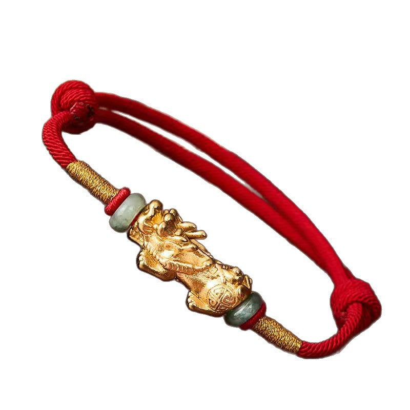Close up of a red woven bracelet with a gold tone Pixiu charm
