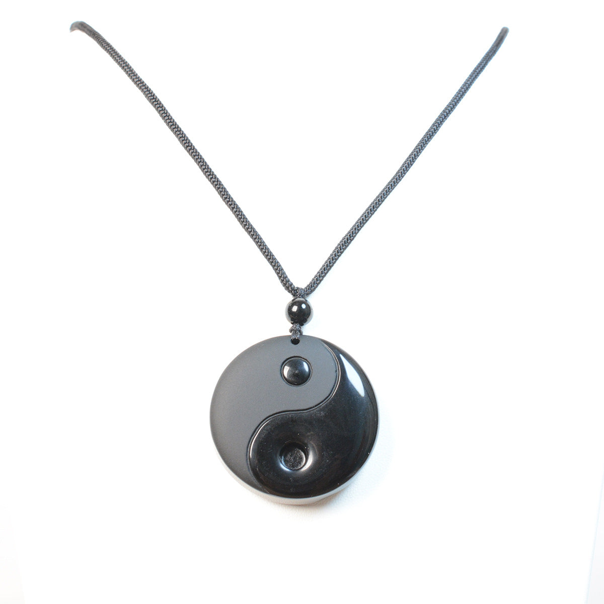 Close up of a round black obsidian pendant with a carved Yin Yang symbol on a black cord