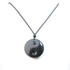 Close up of a round black obsidian pendant with a carved Yin Yang symbol on a black cord