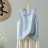 Light blue sleeveless cotton vest hanging on a wooden hanger against a grey wall