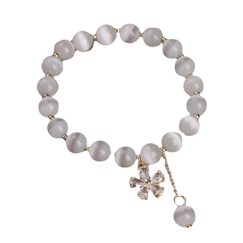 Beige cat's eye bead bracelet with gold flower charm on wooden surface