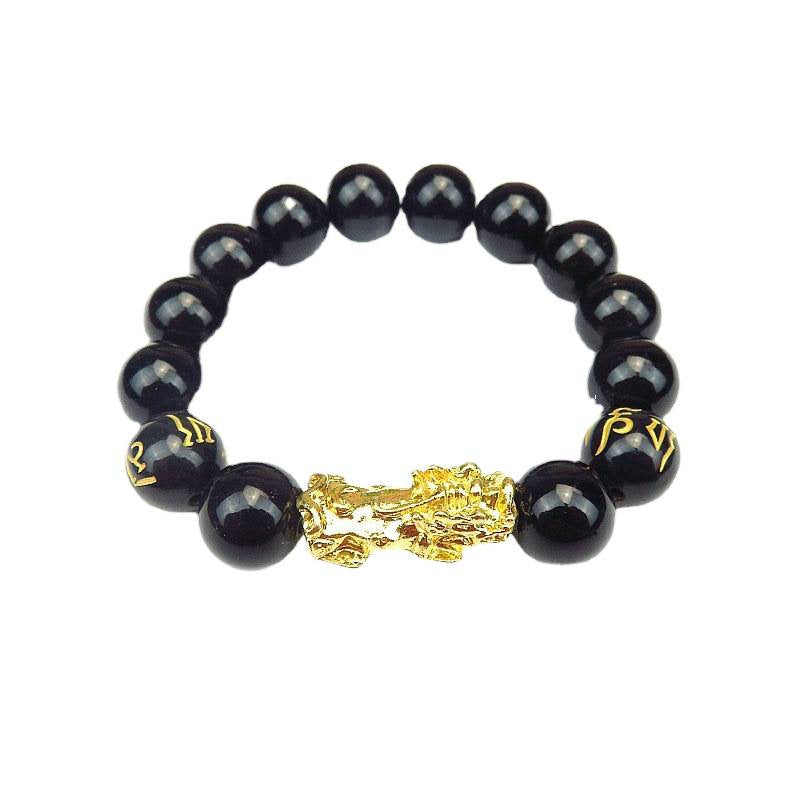 Close-up of a black glass bead bracelet with a gold-tone Pixiu charm and mantra beads on a bamboo surface