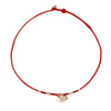 Close up of a thin red braided cord bracelet with a silver coin charm on a wrist