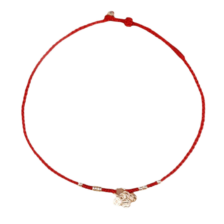 Close up of a thin red braided cord bracelet with a silver coin charm on a wrist