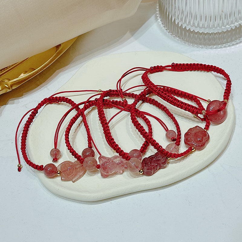 A collection of red string bracelets with pink strawberry quartz charms arranged on a white plate.