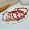 A collection of red string bracelets with pink strawberry quartz charms arranged on a white plate.