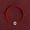 Close up of a red braided bracelet with a silver coin charm on a dark background