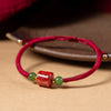 Close up of a red braided bracelet with a square cinnabar bead engraved with mantras