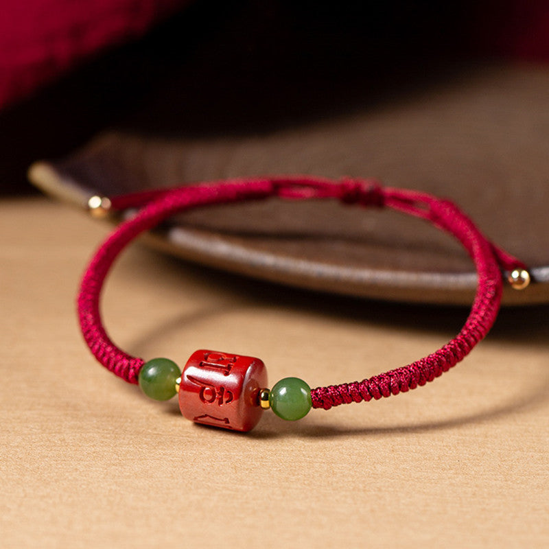 Close up of a red braided bracelet with a square cinnabar bead engraved with mantras