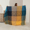 Woman holding up a blue and yellow patchwork chenille throw blanket with fringe