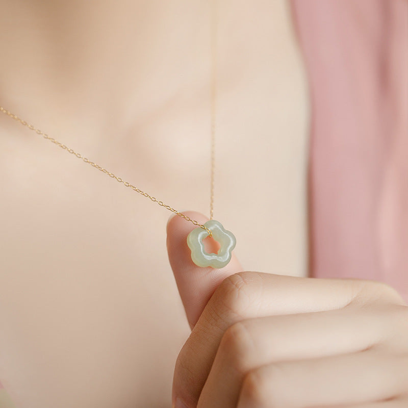 Close up of a hand holding a light green jade flower pendant on a gold chain