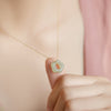 Close up of a hand holding a light green jade flower pendant on a gold chain