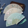 Three open bamboo folding fans with floral prints and tassels on a blue background
