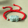 Close up of a light green jade Pixiu charm on a red braided string bracelet