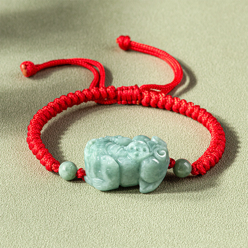Close up of a light green jade Pixiu charm on a red braided string bracelet