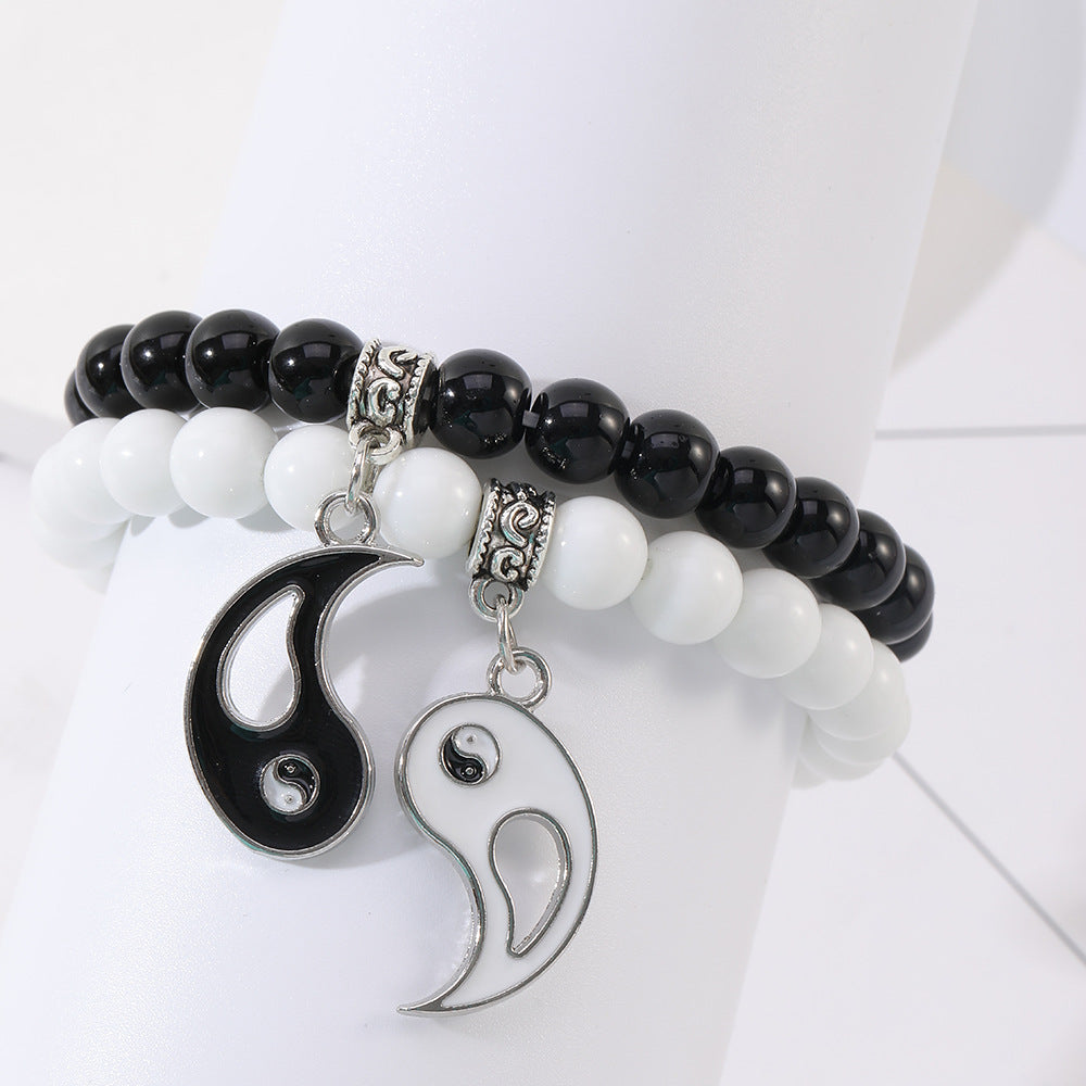 Two beaded bracelets with black and white beads and hanging Yin Yang charms on a wrist display