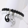 Two beaded bracelets with black and white beads and hanging Yin Yang charms on a wrist display