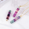 Three natural fluorite cylindrical pendants on gold chains displayed on a white surface