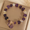 Purple crystal beaded bracelet with a gold money bag charm on a beige box