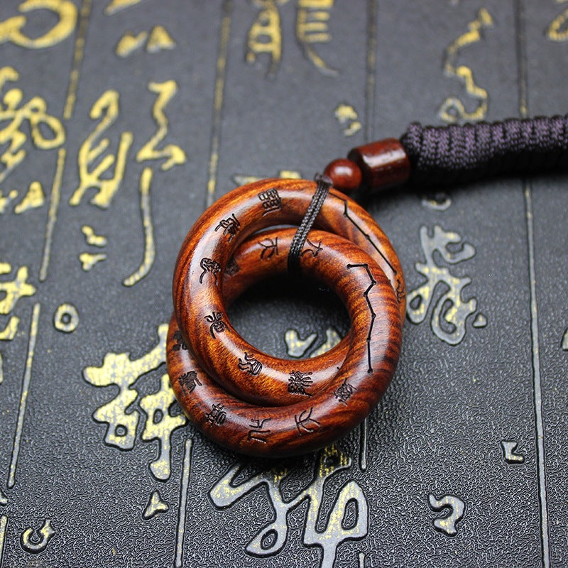 Close up of a brown wooden pendant shaped like two interlocking rings on a dark background.