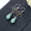 Pair of silver tone dangle earrings with magnolia flowers and light green water drop beads on a dark wood surface