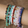 A collection of colorful natural stone disc bead bracelets stacked on a wrist.