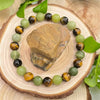 Round beaded bracelet with green jade and brown tiger eye stones on a wooden slice