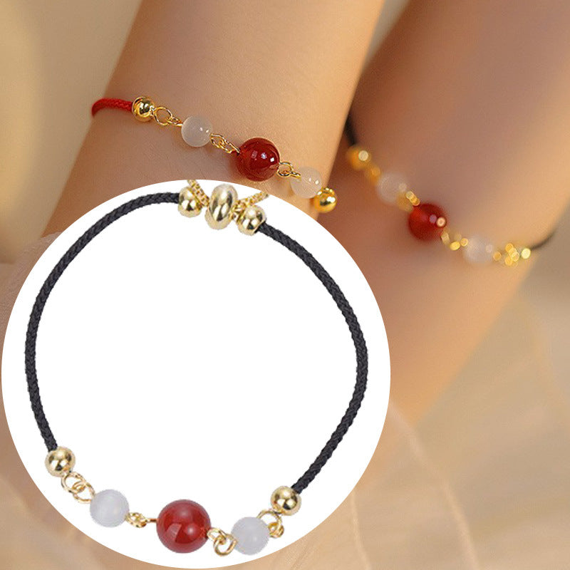 Close up of a black braided bracelet with a red agate bead and gold tone copper accents on a white background