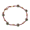 Close-up of a woman's ankle wearing a red woven anklet with green flower beads
