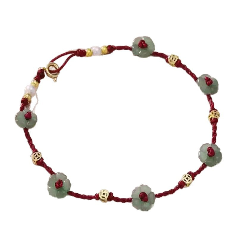 Close-up of a woman's ankle wearing a red woven anklet with green flower beads