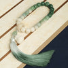 Close up of a green and white gradient bodhi seed wrist mala with a long tassel resting on a wooden surface