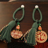 Two brass keychains with red and green woven cords, featuring Fu character charms and tassels on a wooden surface
