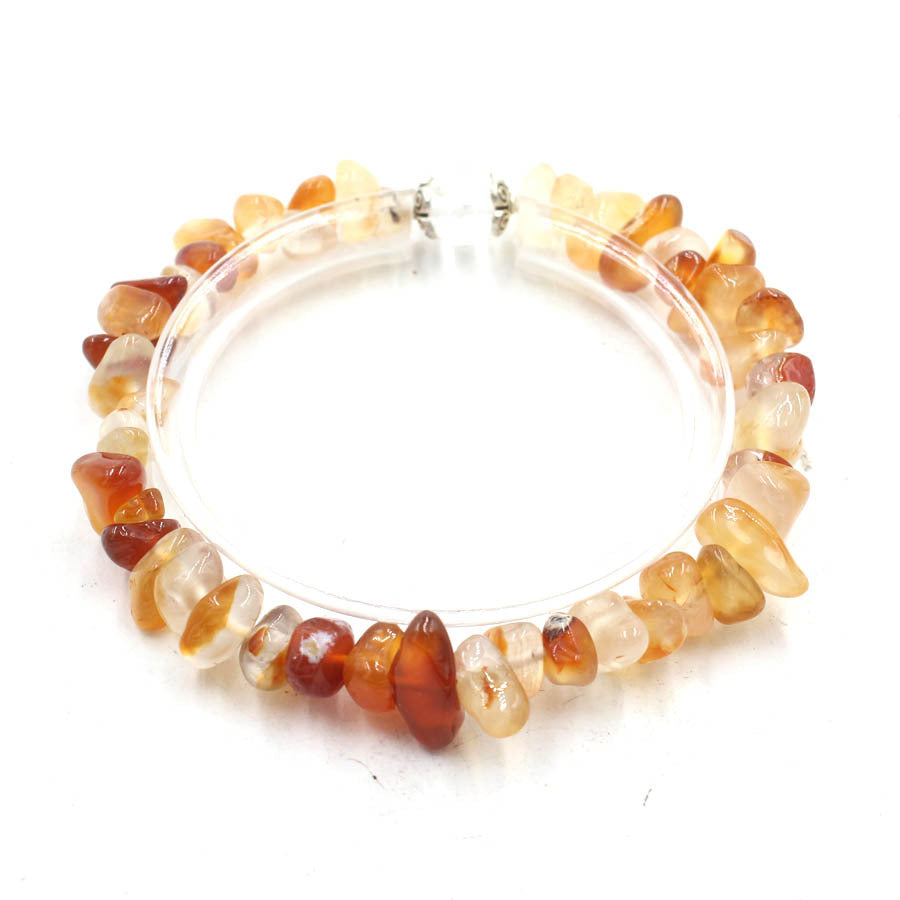 A close-up of a handmade bracelet made from small amber-colored crystal chips on a clear cord.