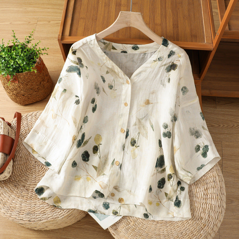 White cotton women's shirt with green plant print hanging on a wooden hanger