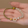 Hand holding a green woven bracelet with white glass beads and a white flower charm.