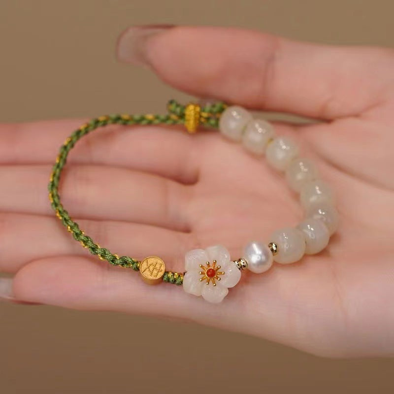 Hand holding a green woven bracelet with white glass beads and a white flower charm.