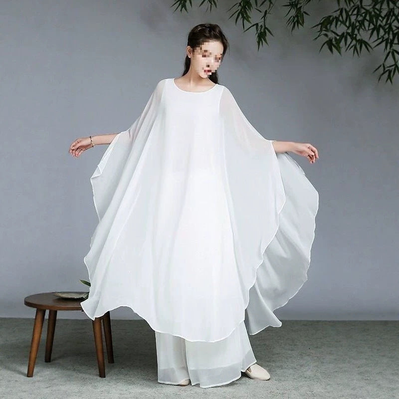 Woman wearing a white flowing tunic and wide leg pants standing in a studio
