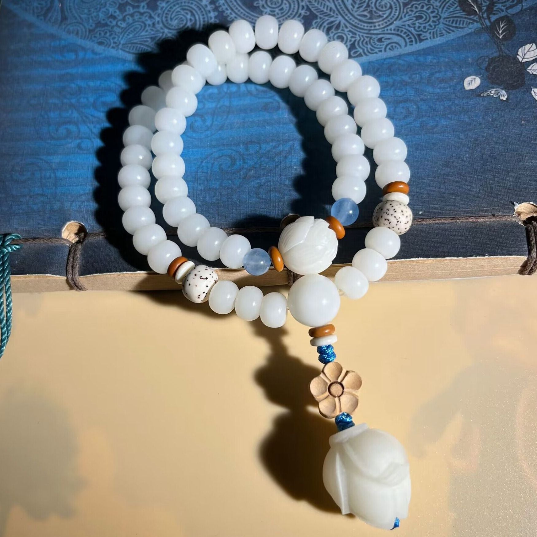 Two-wrap white bodhi seed bracelet with a carved lotus pendant hanging from a blue cord