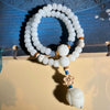 Two-wrap white bodhi seed bracelet with a carved lotus pendant hanging from a blue cord