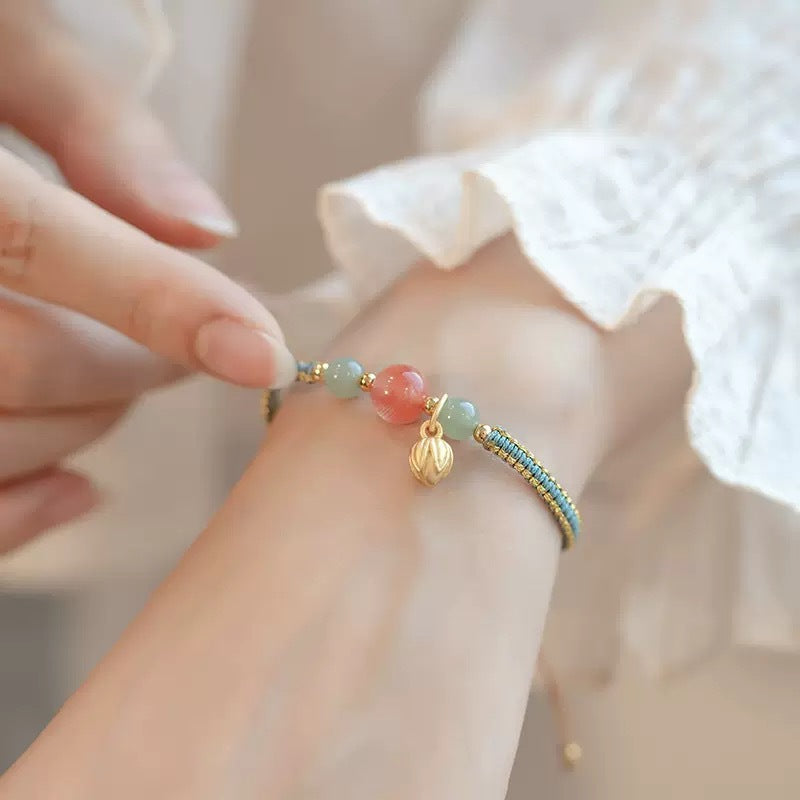 Close up of a green woven bracelet with a gold lotus charm on a wrist