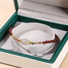 Close up of a red garnet beaded bracelet with a central white oval stone resting in a green jewelry box
