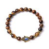 Brown tiger eye beads bracelet with gold tone Hamsa hand and blue evil eye charm on white background