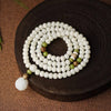 Coiled white bodhi seed bracelet with green accents and a lotus pendant on a dark wooden surface