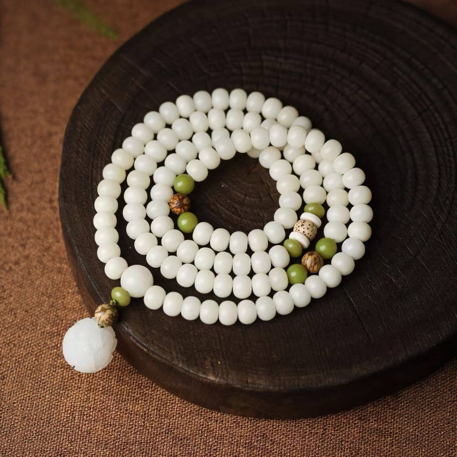 Coiled white bodhi seed bracelet with green accents and a lotus pendant on a dark wooden surface