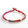 Close-up of a red multicolored woven bracelet with gold tone beads on a white background
