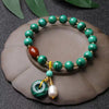 Green malachite beaded bracelet with red agate bead and hanging charm on a dark surface