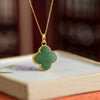 Gold tone four leaf clover necklace with green resin center on a display stand