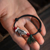 Close-up of a 925 silver koi fish charm on a black and red braided bracelet worn on a wrist.
