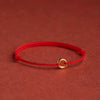 Close-up of a red braided string bracelet with a small gold ring charm on a textured background