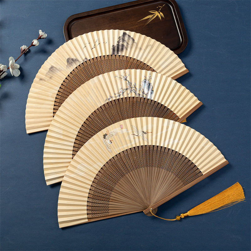 Open bamboo folding hand fan with yellow paper surface showing a painted crane design and a brown tassel